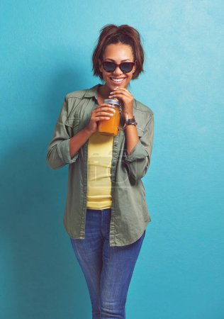 Photo for Happy woman, portrait and sunglasses with orange juice for vitamin C or summer fashion on a blue studio background. Female person, brunette or model with smile for citrus drink or fresh beverage. - Royalty Free Image