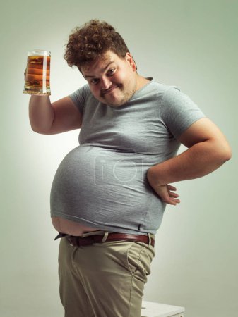 Photo for Obese, weight gain and beer for man in studio with alcohol for unhealthy habit, plus size and humor. Overweight person with glass in hand and fat stomach for cheers and comedy for comic expression. - Royalty Free Image
