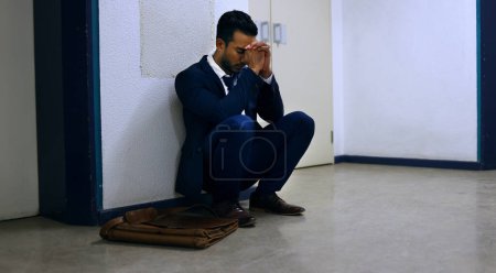 Businessman, fired and stress on floor at workplace with unemployment, failure and disappointment. Professional, employee and concerned in corridor of office building with bag, leaving and helpless.