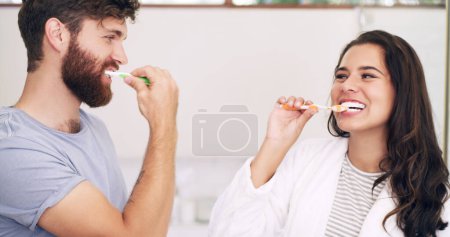 Morning, happy or couple in bathroom brushing teeth together in grooming routine with love in home. Woman, oral health or man cleaning mouth with toothbrush, smile or toothpaste for dental wellness.