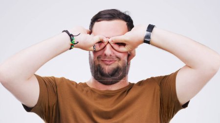 Photo for Studio, man and binoculars with hands for crazy comic, silly and goofy expression with smile. Face, male model and goggles sign, symbol and emoji for feedback or reaction by white background. - Royalty Free Image