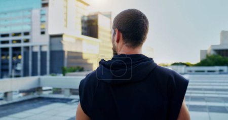 Photo for Back, training and man thinking in city for running, cardio workout or endurance exercise. Lens flare, sports and athlete for parkour preparation, fitness or thoughtful on rooftop in urban town. - Royalty Free Image
