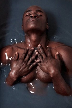 Photo for Black man, bathing and charcoal water with eyes closed for skincare, detox and anti aging or ph level. Male person, muscular and dark liquid in bath for art deco, beauty and abstract creativity. - Royalty Free Image