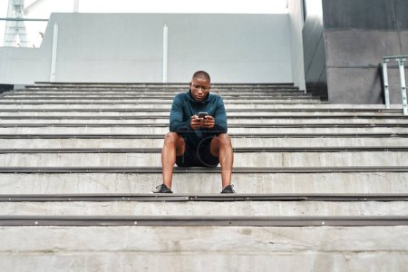 Photo for African man, smartphone and sports, stairs and stadium for training, outdoor or workout on stands for wellness. Male athlete, technology and break in exercise for tournament, competition or contest. - Royalty Free Image