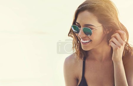 Mujer, gafas de sol y sonrisa para vacaciones en la playa en bikini para tomar el sol vacaciones en la isla tropical, viajes o verano. Persona femenina, felicidad y paraíso de fin de semana en Miami o explorar, relajarse o viajar.