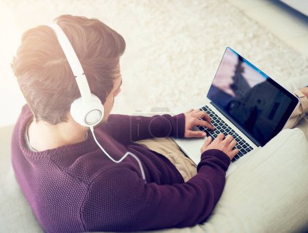 Photo for Man, laptop and music on sofa in home with top view for audio streaming, subscription service and online gaming. Person, headphones and typing on tech app for sound entertainment, radio and playlist. - Royalty Free Image