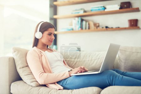 Photo for Woman, laptop and headphones with video on sofa in home for audio streaming, subscription service and social media. Person, music and watching series with movie entertainment, radio playlist or sound. - Royalty Free Image
