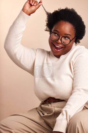 Téléchargez les photos : Femme noire, sourire et soins afro en studio avec fierté, excité et soin des cheveux sur fond beige. Plus la taille, la personne féminine et la croissance des cheveux pour le bien-être, revitalisant et traitement à l'huile chaude avec des lunettes. - en image libre de droit