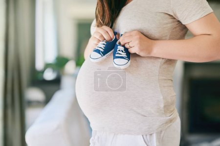 Photo for Pregnant, woman and shoes on belly in home for reveal of boy gender with blue color, journey and experience of pregnancy. Mother to be, holding sneakers and stomach for love or bonding and motherhood. - Royalty Free Image