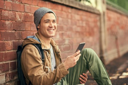 Photo for Asian man, cellphone and city travel or brick wall for outdoor tourism in China or texting, communication or smile. Male person, smartphone and location search on mobile app, journey or direction. - Royalty Free Image
