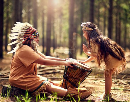 Chef amérindien, femme et tambour dans la nature avec enfant pour la musique, la connexion et l'apprentissage de l'histoire de la tribu. Instruments, mère et fille avec rythme pour la culture, l'enseignement et le guide spirituel.