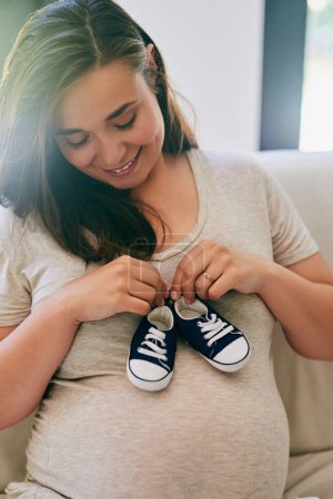 Joyeux, femme enceinte et chaussures sur le ventre à la maison pour révéler le sexe du garçon, voyage et expérience de la grossesse. Mère à être, tenant des baskets et l'estomac pour l'amour ou le lien et la maternité avec soin.