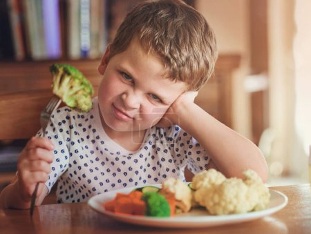 Photo for Upset, young boy and reject food at dinner table for not eating vegetable and no to nutrition at home. Healthy, child and face with disgust for portrait or refuse balanced diet for fussy eater. - Royalty Free Image