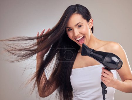 Foto de Mujer asiática, secador de pelo y feliz con retrato en estudio para el crecimiento, enderezar y tratamiento brasileño sobre fondo gris. Persona femenina, emocionada y orgullosa con cabello limpio, queratina y peinado. - Imagen libre de derechos