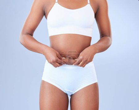 Photo for Woman, body fat and lose weight with underwear for diet or nutrition on a blue studio background. Stomach or belly of female person or model touching skin in detox, liposuction or health and wellness. - Royalty Free Image
