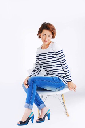 Photo for Fashion, chair and portrait of girl in studio for sweater style, trendy clothing and jeans with white background. Smile, relax and person for happiness, confidence or comfortable outfit on mockup. - Royalty Free Image