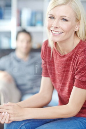 Foto de Disfrutando del estilo de vida casual. Retrato de una atractiva joven sentada en la sala de estar con su novio en el fondo - Imagen libre de derechos