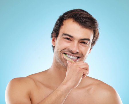 Portrait, brushing teeth and man with dental hygiene, wellness and grooming routine on blue studio background. Face, person or model with oral health, cleaning mouth or remove plaque for fresh breath.
