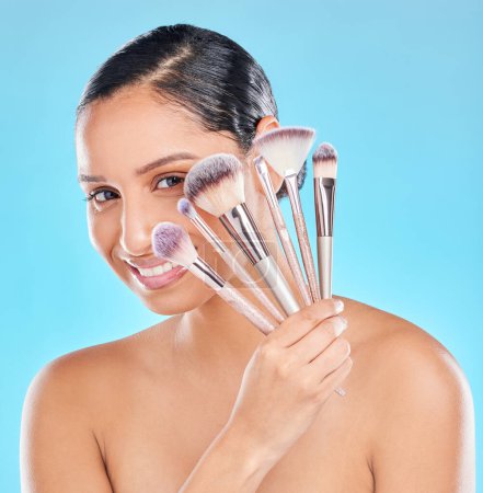 Photo for Creative, makeup and portrait of girl with brushes in hand to apply cosmetics in blue background. Studio, beauty and artist with tools set for application of foundation, powder or skincare with smile. - Royalty Free Image