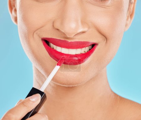 Photo for Woman, mouth and apply lipstick in studio, red lips and cosmetics makeup on blue background. Female person, beauty and confident smile for glossy grooming, skin care and makeover transformation. - Royalty Free Image