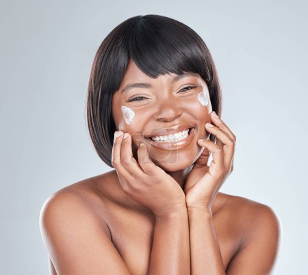 Photo for Skincare, happy and black woman with face cream application in studio for wellness, shine or cosmetics on grey background. Beauty, sunscreen and portrait with anti aging, lotion or collagen facial. - Royalty Free Image