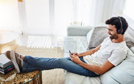Photo for Home, man and smartphone with headphones on couch for listening to music, radio and networking. Living room, male chatter and mobile app for streaming podcast, online games and social media to relax. - Royalty Free Image