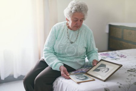 Photo for Memory, frame and elderly woman on bed with picture for melancholy, family history and nostalgia. Senior person, lonely and retirement with photo at home for grief, remember and reminisce of husband. - Royalty Free Image