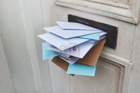 Door, letter and mail or envelope in box of home for communication or notice, stacked and overflowing with documents. Mailbox, post and address for mortgage or debt, message and paper from bank