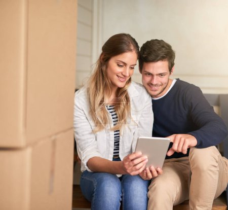 Photo for Happy couple, new home and browsing with tablet by boxes for moving in, renovation or relocation. Young man and woman with smile on technology for house decor, ideas or furniture for interior design. - Royalty Free Image