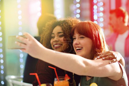 Foto de Mujeres, selfie y cóctel con luces para chicas noche con happy hour en Londres con amigos. Redes sociales, recuerdos y alcohol en discoteca para bebidas con felicidad, sonrisa y fin de semana - Imagen libre de derechos