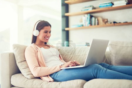 Photo for Woman, laptop and happy with headphones on sofa in home for audio streaming, subscription service and social media. Person, music and watching series with movie entertainment, radio playlist or sound. - Royalty Free Image