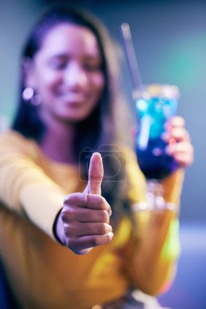 Woman, glass and thumbs up in party for celebration with cocktail, agreement and good review for nightclub. Female person, alcohol and hand with yes emoji in pub for promote concert and event winner.