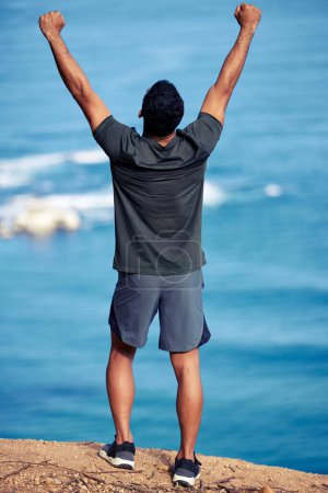 Photo for Man, exercise and mountain celebration at cliff with fist for hiking victory or outdoor view, back or workout. Male person, trekking and health goals at ocean or explore Australia, journey or winner. - Royalty Free Image