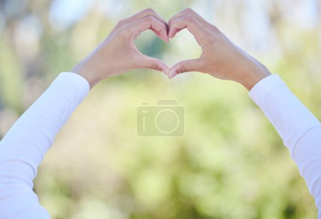 Foto de Outdoor, hands and heart with woman, care and kindness with icon, symbol for love and promotion. Closeup, person and girl in park, gesture and peace with emoji, support and summer with gratitude. - Imagen libre de derechos
