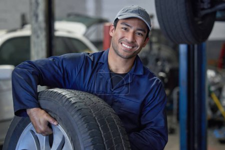 Man, mechanic and car maintenance with tire change for fixing wheel in garage for vehicle repairs. Male person or technician and smile for motor inspection, road validation and routine service.