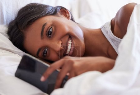 Frau, telefonieren und SMS schreiben am Morgen, lesen und wachen mit einem Lächeln zur Benachrichtigung, zum Chat oder Online-Dating zu Hause auf. Mädchen, Mensch und glücklich mit Smartphone, Anwendung und Mobilfunknetz im Schlafzimmer.