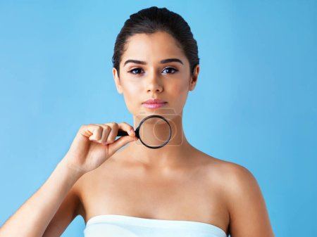 Beauty, portrait and girl with magnifying glass in studio for skincare, treatment or results inspection on blue background. Skin, magnifier or gen z model with chin search for pcos facial hair growth.