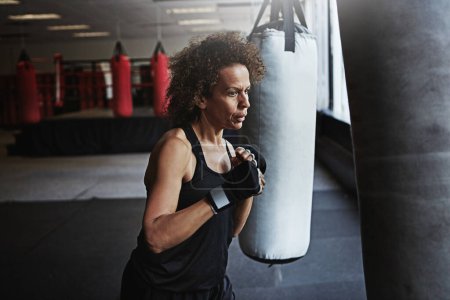 Photo for Gym, punching bag and mature woman in boxing for workout, challenge or competition training. Power, muscle and strong champion boxer in exercise with confidence, fight and energy in MMA sports club - Royalty Free Image