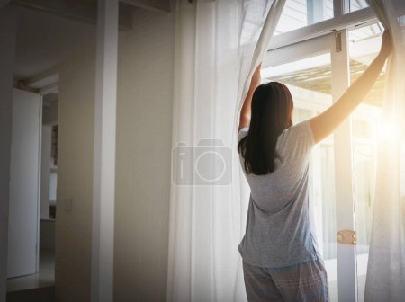 Foto de Back, woman and open curtain in morning, window and fresh wake up with sunrise in hotel ready for day. Routine, outside view and nature on holiday or weekend, drapes and light in apartment in bedroom. - Imagen libre de derechos