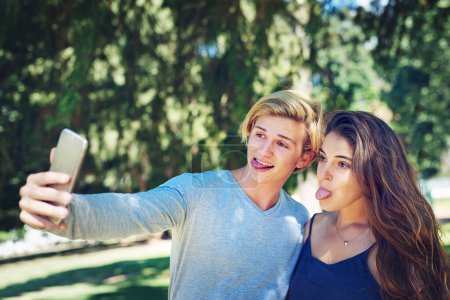 Téléchargez les photos : Couple, selfie et drôle visage avec la langue au parc avec collage, en plein air et drôle sur le web à l'université. Homme, femmes et étudiants pour la photographie, la mémoire et la bande dessinée avec poste sur les médias sociaux à l'université. - en image libre de droit