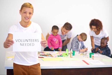 Volunteers needed, portrait and child with sign in daycare for help, community service or charity. Outreach, poster and teen boy with people for support, nonprofit NGO or giving back to orphanage.