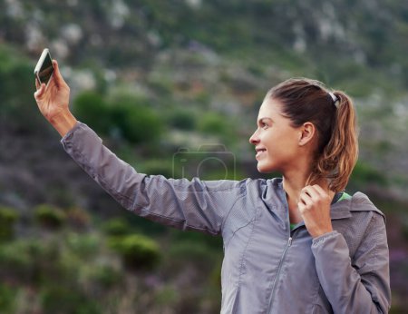 Woman, runner and selfie in nature for fitness update, progress or social media post on mountains. Young person or sports influencer with photography on mobile for running, hiking or trekking outdoor.