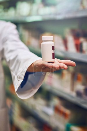 Téléchargez les photos : Pharmacist, hand and bottle for pills in store with by shelf for stock, show and inventory for wellness. Person, employee and container with pharmaceutical, review and presentation for drugs at shop. - en image libre de droit