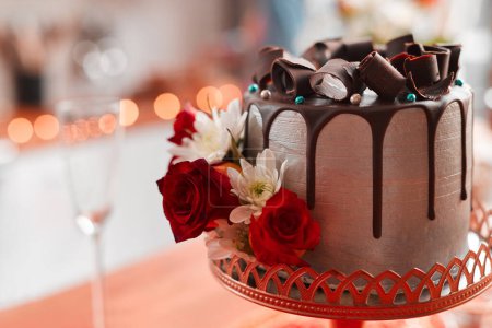 Photo for Chocolate cake, red and roses for wedding reception on pedestal for celebration, social event and dessert. Luxury, cocoa and frosting with flowers for decoration, sweet and confectionary for party. - Royalty Free Image
