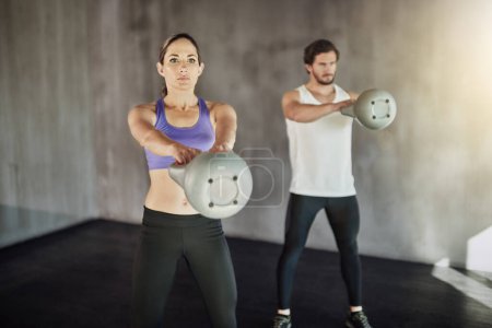 Foto de Training, sports and couple in gym with kettlebell, power and workout challenge together at fitness club. Man, woman and personal trainer with weights, muscle development and healthy body exercise - Imagen libre de derechos