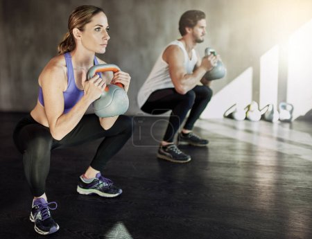 Squat, man and woman in gym with kettlebell, fitness and power training at workout challenge together. Couple, sports club and personal trainer with weights, muscle development and body exercise