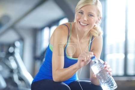 Téléchargez les photos : Earphones, water and portrait of woman athlete in gym listening to music, radio or podcast. Smile, fitness and female person with h2o drink for hydration with sports exercise, workout or training - en image libre de droit