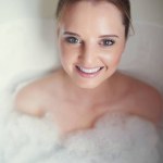 Woman, bubbles and portrait in bathroom tub for hygiene, cleaning and cosmetics with wellness in home. Girl, person and washing with soap, foam and happy in water to stop bacteria in morning at house.