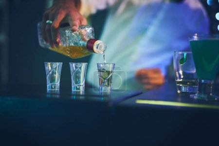 Barman, bouteille et verser dans des verres de tir à la boîte de nuit pour le service, commande et serveur de comptoir avec hospitalité. Barman, employé et main avec préparer les esprits dans le verre à l'événement social et happy hour.