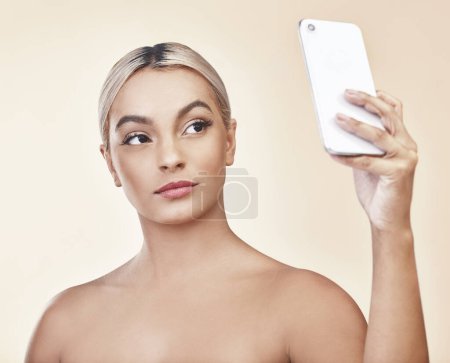 Selfie, femme et maquillage pour la beauté en studio sur fond de campagne et post médias sociaux. Femme, confiance et influence avec confiance ou satisfait des cosmétiques et de l'élégance.